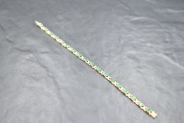 A 9ct gold articulated bracelet having oval emerald coloured stones interspersed by diamond chips,