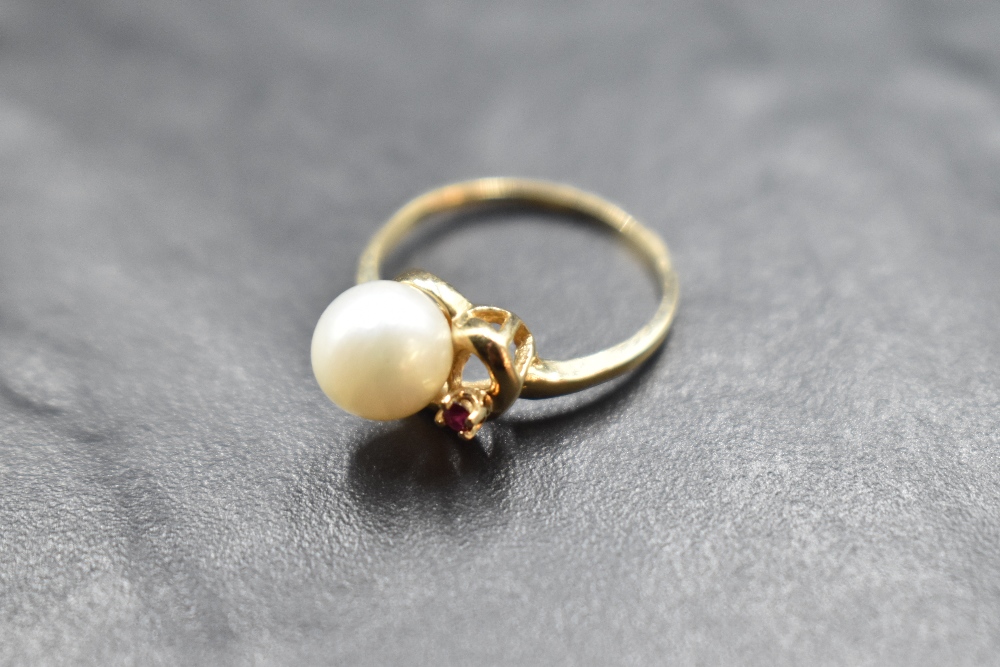 A cultured pearl ring with ruby chip set swirl mount on a yellow metal loop stamped 10K, size N &