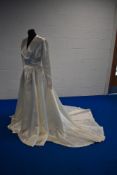 A vintage 1950s cream satin wedding dress, having gathered bodice, long sleeves and long train, with