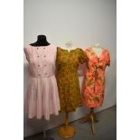 Three vintage 1960s dresses, including olive green linen dress with floral print and pale pink dress