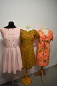 Three vintage 1960s dresses, including olive green linen dress with floral print and pale pink dress