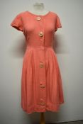 A 1950s coral pink bark cloth day dress, having large buttons to front and pleated skirt, medium