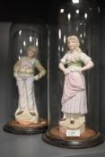 A pair of 19th century German bisque porcelain figures under glass domes.
