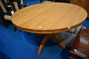 A modern golden oak extending dining table on turned pedestal with butterfly centre leaf, diameter