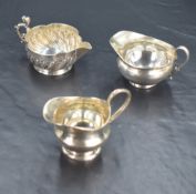A group of three silver cream jugs, one of lobed circular form with half spiral fluting and scrolled
