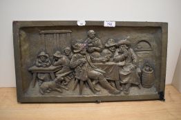 A resin moulded wall plaque, depicting a Dutch tavern scene, measuring 25cm x 50cm overall