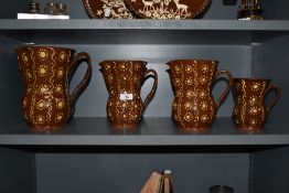 Four 19th Century slipware jugs of graduating sizes, the largest measuring 23cm tall