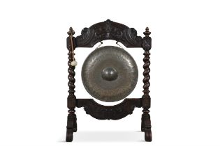 A CARVED AND STAINED OAK FRAMED BRASS DINNER GONG AND BEATER the frame with all over