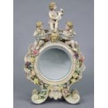 A circular dressing table mirror in porcelain figural frame, a cherub to each side,