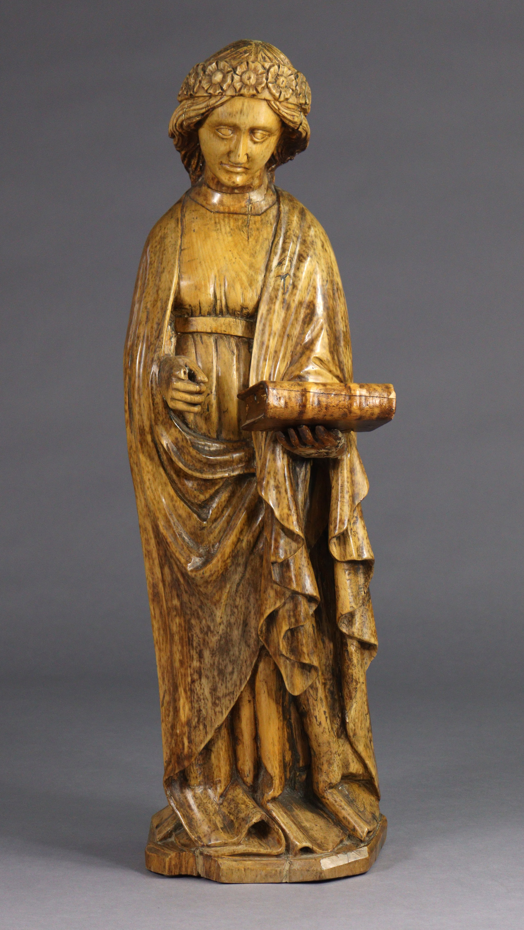 A carved limewood figure of St. Catherine, wearing floral crown, holding a book in her left hand (