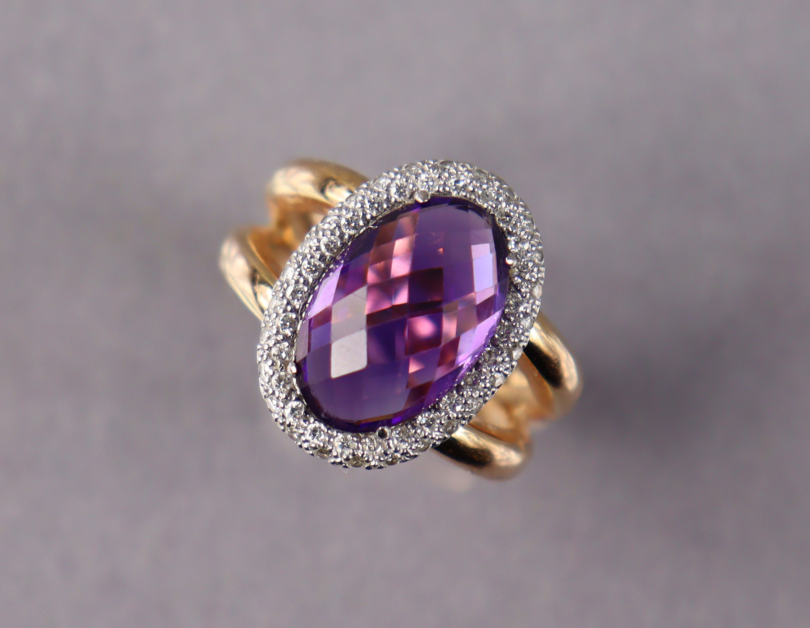 An 18ct gold ring set oval facet-cut amethyst within a border of small diamonds, size M. (7.9g)