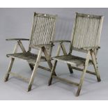 A pair of teak slatted reclining garden elbow chairs.
