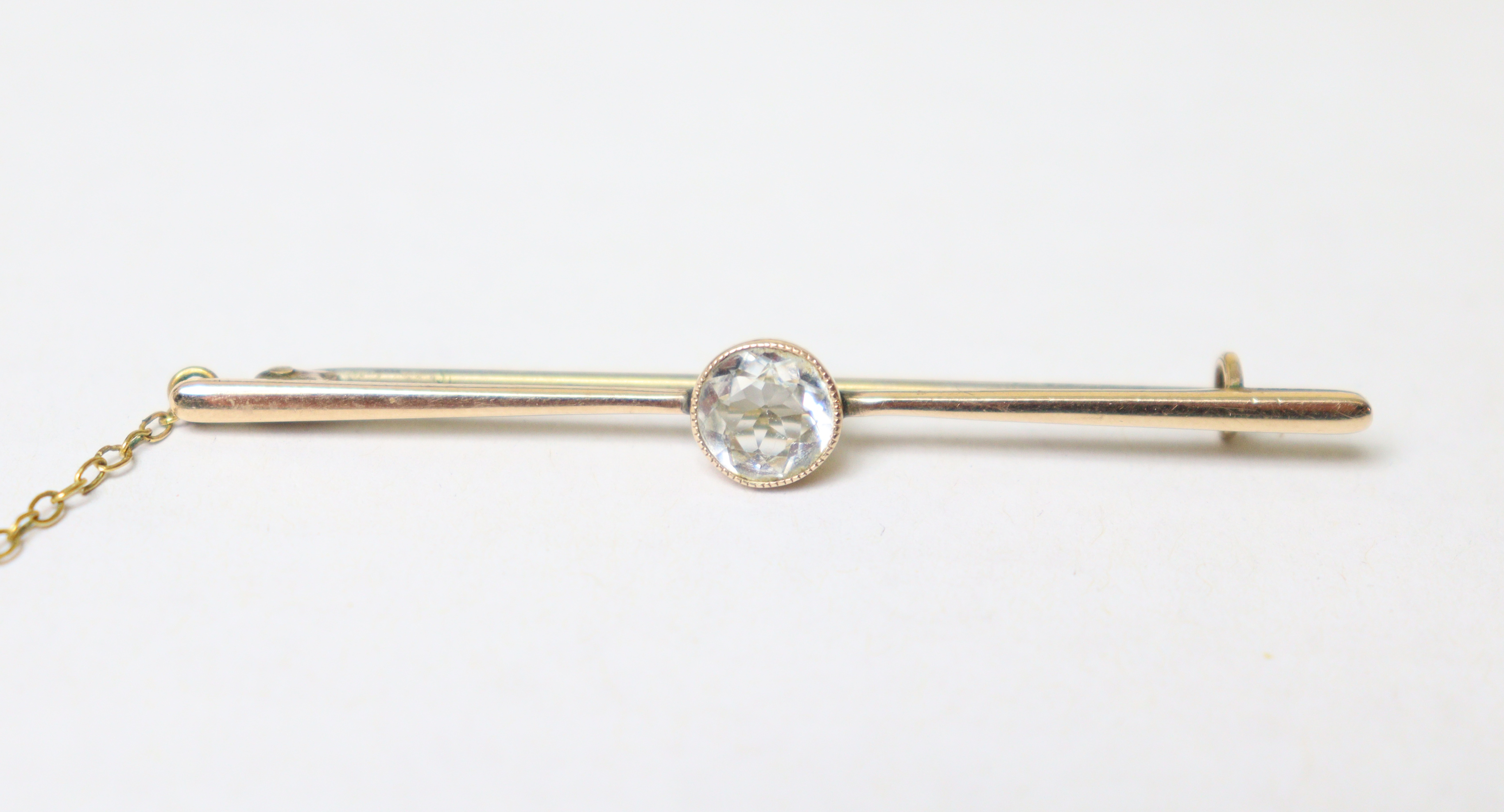 A 9ct gold bar brooch set round-cut white stone, 2¼” long (2.9g), with safety chain.