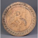A terracotta circular plaque with moulded relief decoration of putti riding a dolphin in folate