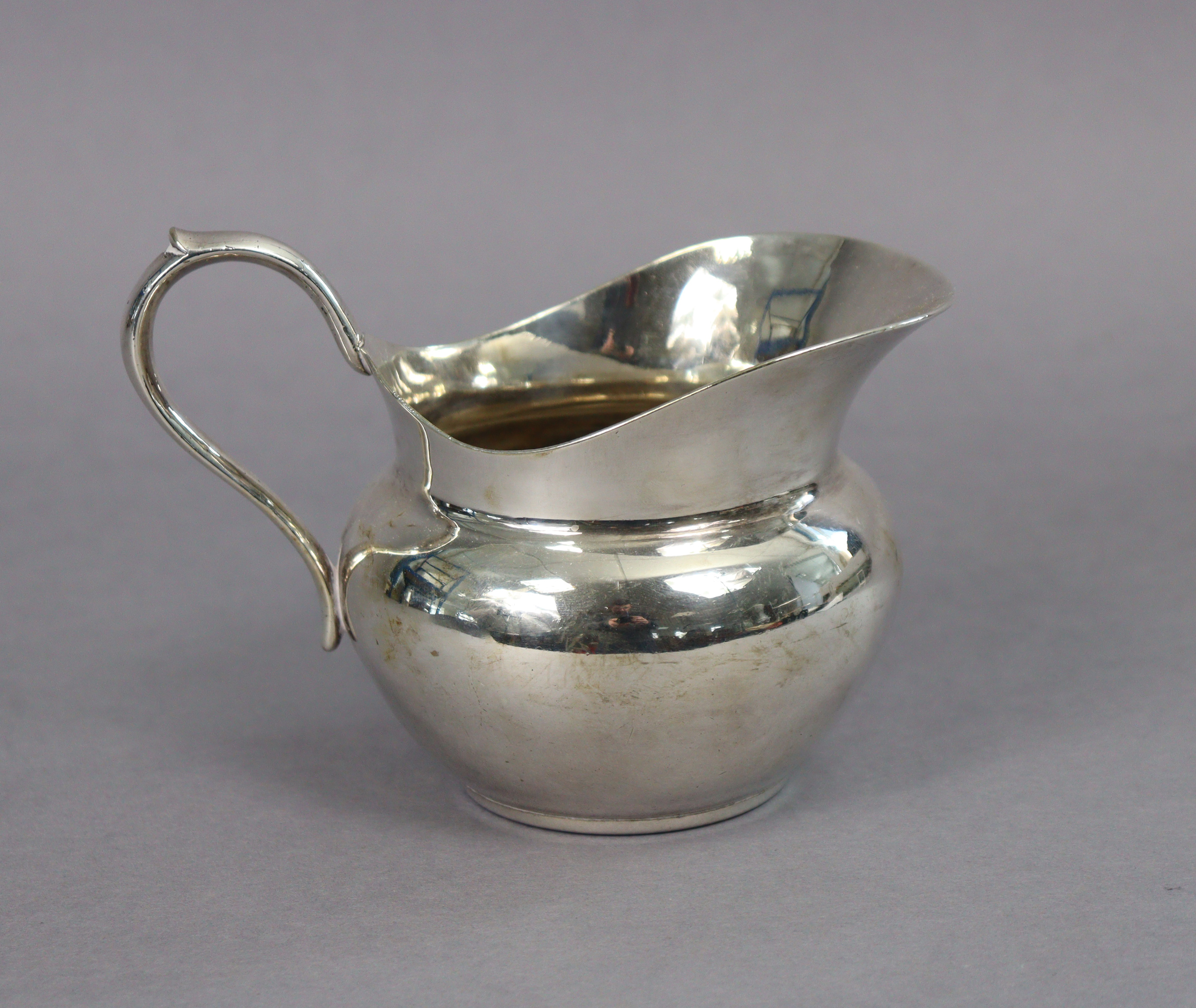 An early 20th century Christofle silver-plated cream jug of ovoid form, with scroll handle & wide