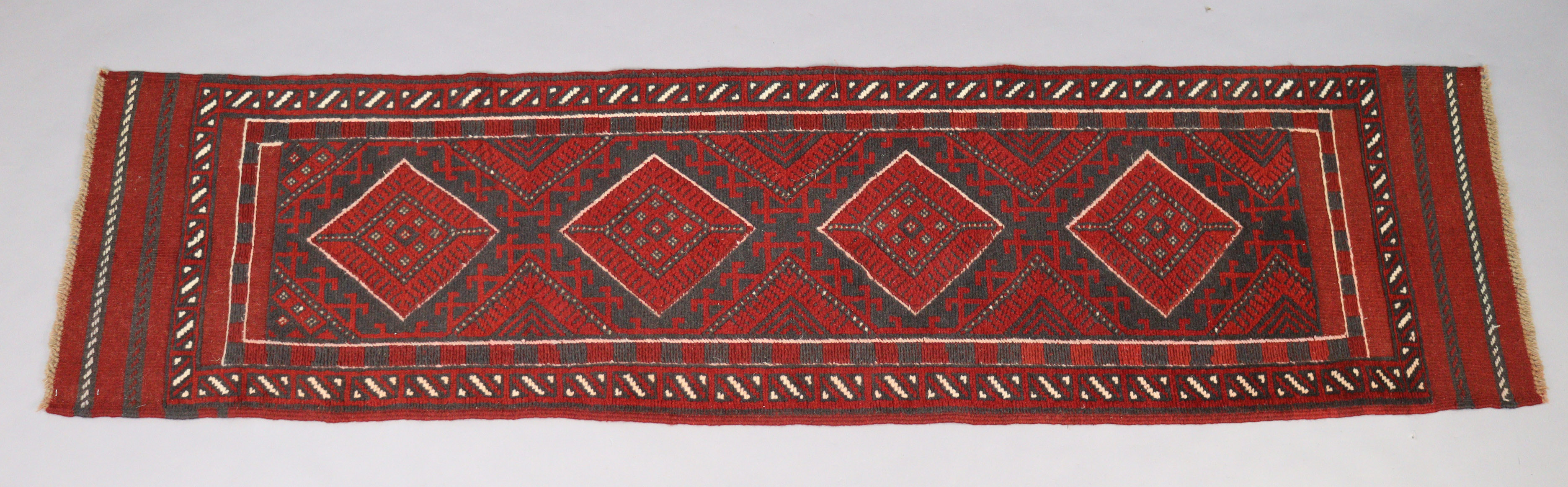 A Meshwari runner of madder ground with repeating geometric design in narrow borders, 23” wide x 97”