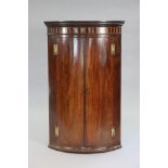 A George III mahogany bow-front hanging corner cupboard with inlaid & ebonised decoration to the