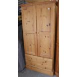 A pine wardrobe enclosed by a pair of panel doors above two long drawers, & on a plinth base, 35”