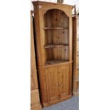 A pine tall standing corner cabinet fitted three shaped open shelves above a cupboard enclosed by
