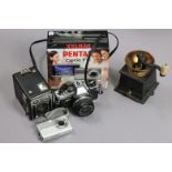 An Olympus “OM10” camera; a Kodak “Six-20 Brownie D” box camera; a Pentax “Optio” camera; & a