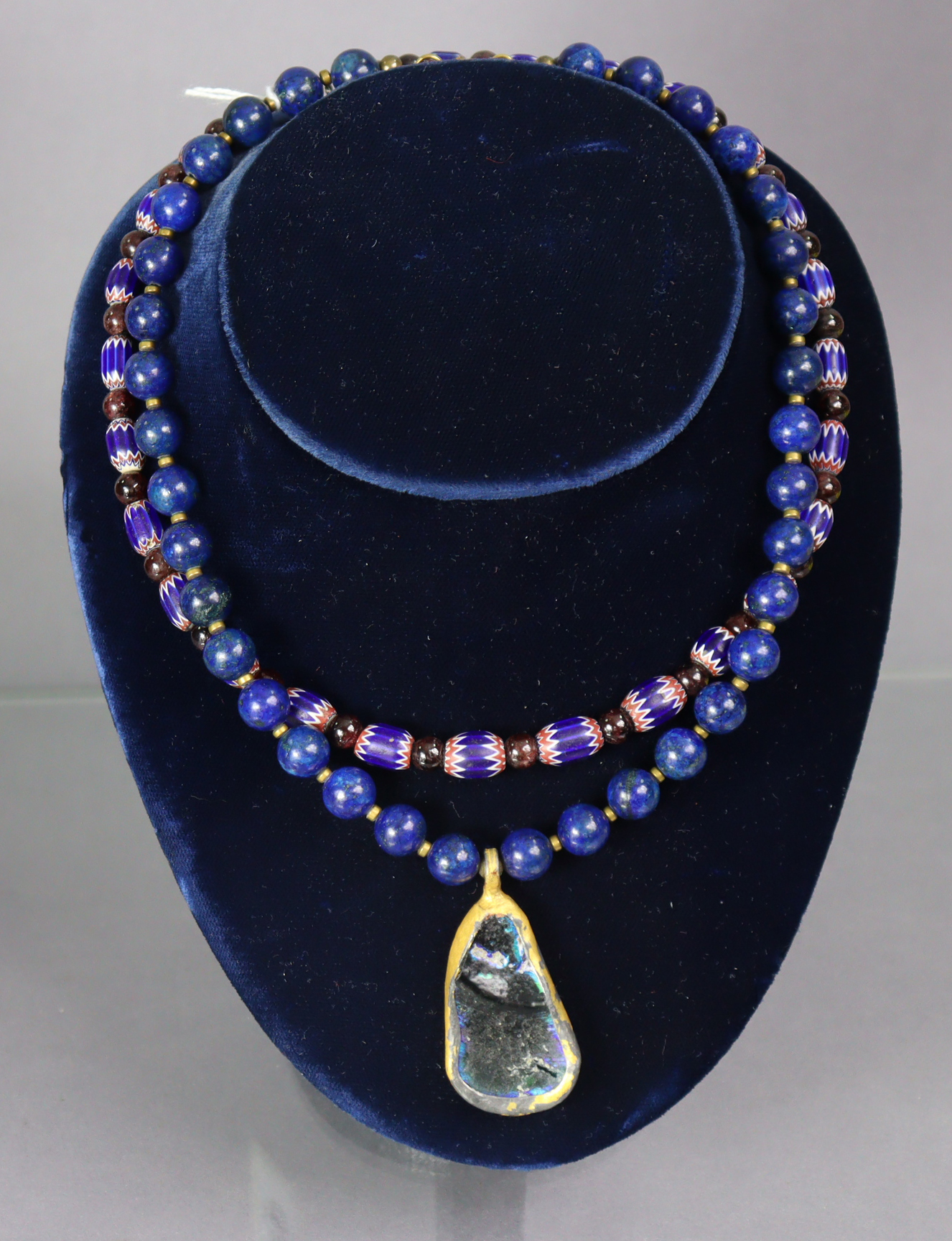 A necklace of lapis lazuli spherical beads with asymmetrical pendant of a fragment of iridescent