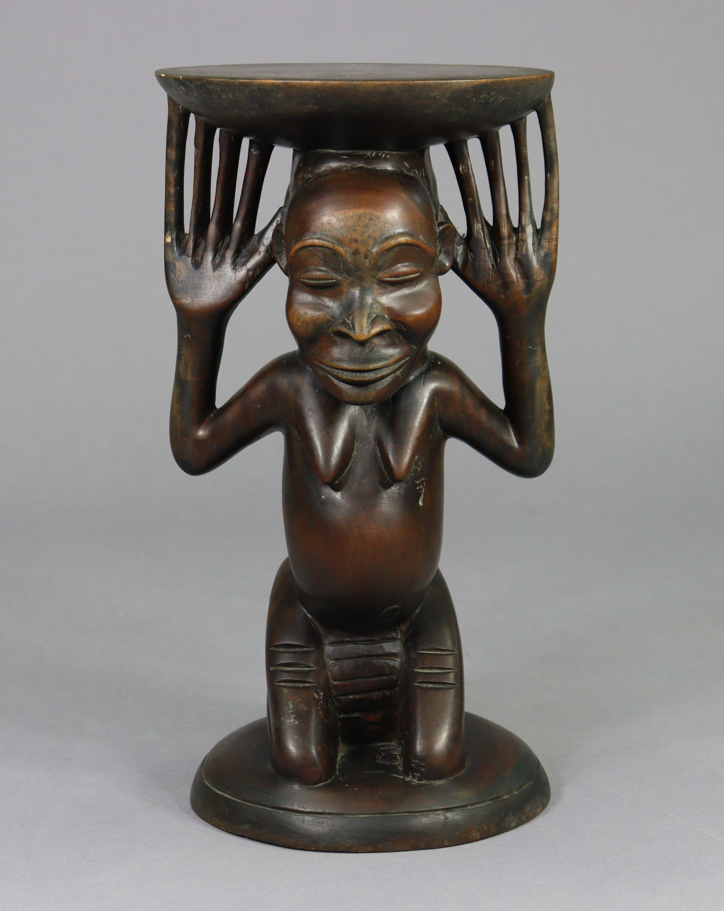 A Luba stool, the female figural support kneeling on circular base, her raised hands supporting