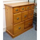 A pine chest fitted with an arrangement of nine drawers having brass cup handles, & on a plinth