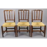 A set of three early 20th century splat-back dining chairs each with a woven-rush seat, & on