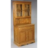 A pine dresser the upper part fitted shelf enclosed by a pair of glazed doors above an open recess