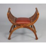 A 20th century hardwood stool with ‘X’ shaped supports, with padded red leather seat, 62cm wide x