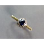 A yellow metal ring set round-cut sapphire within a border of small diamonds, the shank marked “