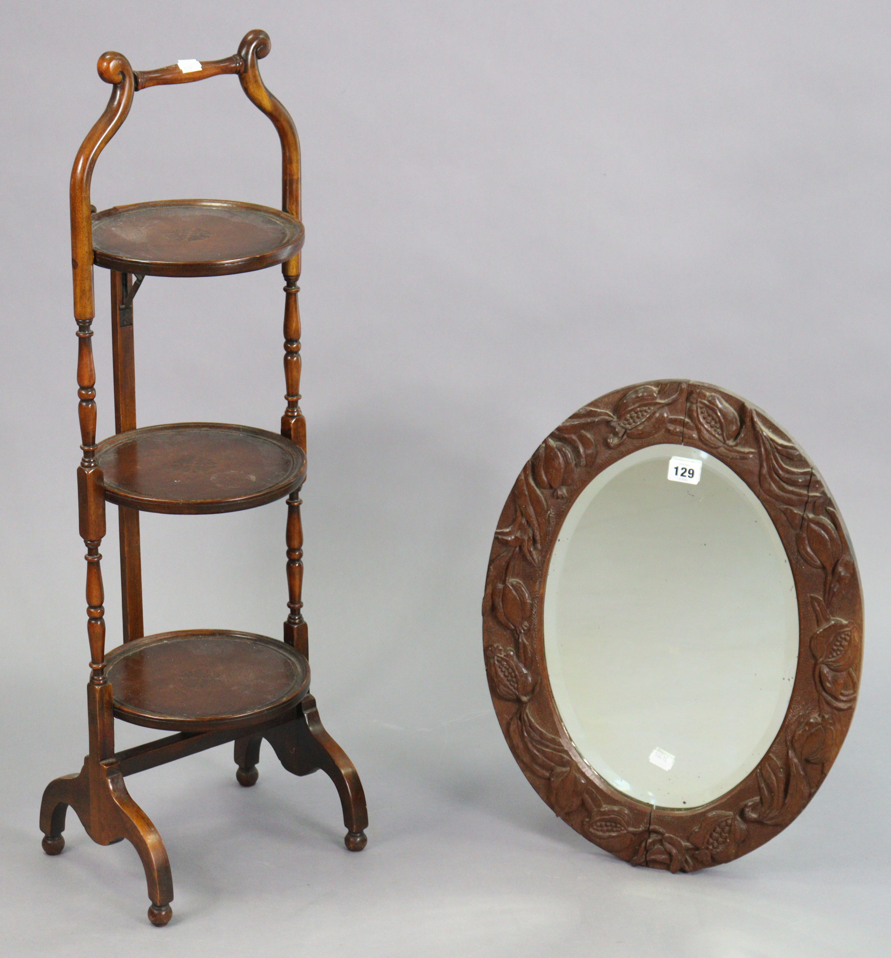 A carved wooden oval wall mirror inset with a bevelled plate, 21” x 15¼”; together with a three-tier