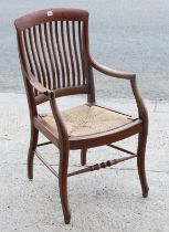 An early 20th century beech comb-back elbow chair with woven-cane seat, & on shaped legs with a
