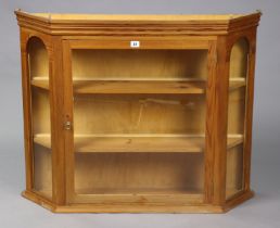A pine wall cabinet having canted sides & fitted two shelves enclosed by a glazed door & glazed