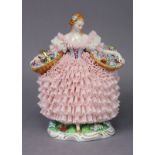 A Sitzendorf porcelain figure of a flower girl, with basket of flowers to each side upon her pink