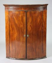 A Georgian inlaid mahogany bow-front hanging corner cupboard fitted three shelves enclosed by a pair