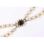 A two-row necklace of graduated cultured pearls, the 9ct gold oval clasp set garnet within a