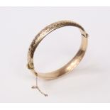 An Edwardian 9ct. gold stiff hinged bangle with engraved foliate decoration to one side;