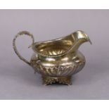 A George IV silver milk jug of squat round semi-fluted form with gadrooned rim & acanthus scroll