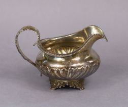 A George IV silver milk jug of squat round semi-fluted form with gadrooned rim & acanthus scroll