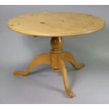 A pine pedestal dining table with a circular tilt top, & on a vase-turned centre column & three
