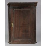 A 19th century mahogany hanging corner cupboard fitted three shaped shelves enclosed by a panel door