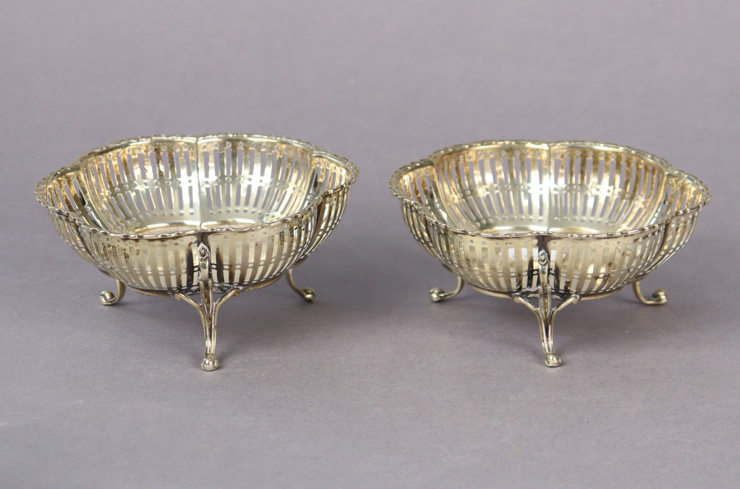 A pair of George V silver sweetmeat dishes each with a pierced border & on three slender legs,