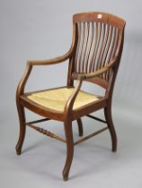 An early 20th century beech comb-back elbow chair with woven-cane seat, & on shaped legs with a