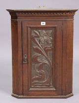A 19th century oak hanging corner cupboard fitted centre shelf enclosed by a carved floral panel