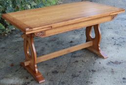 An oak draw-leaf dining table on pierced & shaped end supports joined by a plain centre stretcher; &