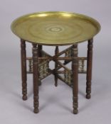 A vintage eastern brass engraved circular occasional table on a hardwood folding stand, 57.5cm