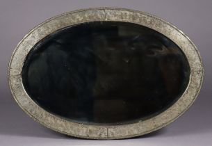 An early 20th century oval wall mirror in hammered-metal frame with embossed decoration, cm x cm.