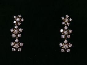 A pair of diamond pendant earrings, each designed as a vertical row of three florets set small round