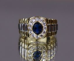 A silver-gilt dress ring set oval-cut blue cubic zirconia within a border of ditto white stones,